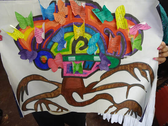 Photo of a dream tree created by cohort member Evelyn. It is a very large drawing done with markers that has all the colors of the rainbow, with multi-colored butterflies attached to the crown of the tree. Dreams are written on the butterflies.