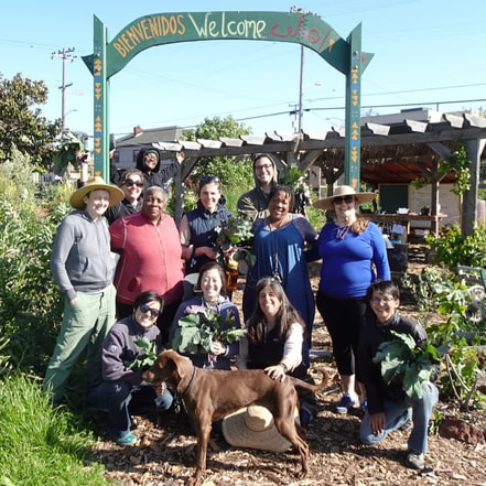 Group picture in a community garden, under a wooden arch that says 